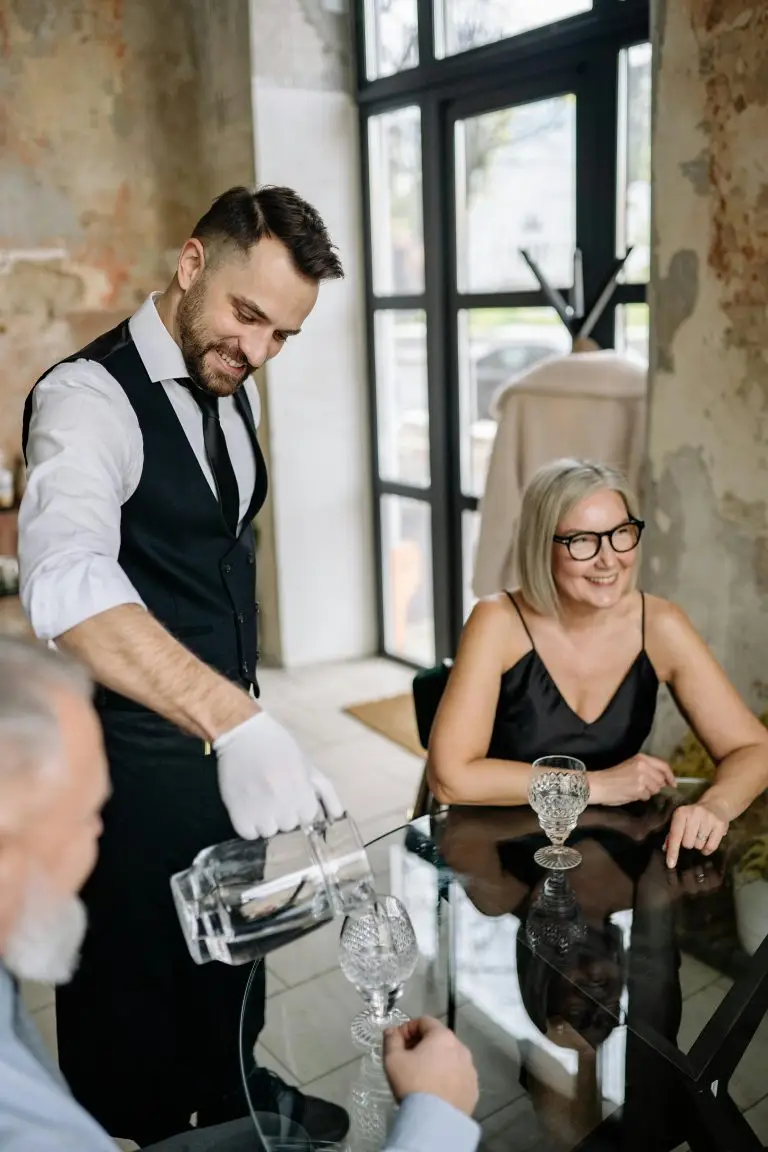 Smiling waiter serves elderly couple in stylish restaurant setting.